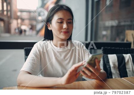 Portrait of asian woman enjoying using mobile phone sitting at outdoor cafe Portrait of asian woman enjoying using mobile phone sitting at outdoor cafe 79702387