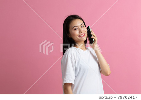 Smiling asian woman speaking mobile phone standing on pink background. Smiling asian woman speaking mobile phone standing on pink background. 79702417