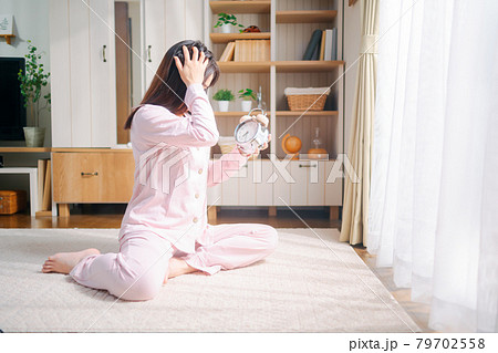 目覚まし時計を見ながら慌てるパジャマの女性　 79702558
