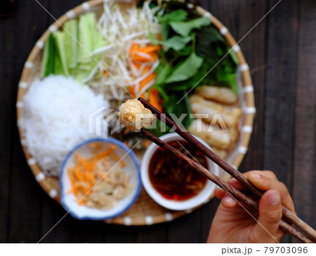 people hold chopsticks pick up fried spring rolls on tray of Vietnamese vegan food 79703096