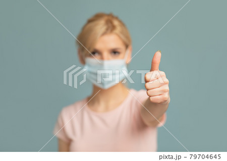 Woman in medical protective mask showing thumb up on grey studio background. Stay safe and healthy during pandemic Woman in medical protective mask showing thumb up on grey studio background. Stay safe and healthy during pandemic 79704645