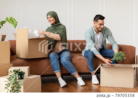 Happy man and woman in hijab packing or unpacking boxes 79705358