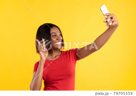 African American Lady Making Selfie Gesturing Victory Sign, Yellow Background 79705359