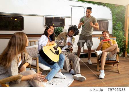 Group of diverse young friends having outdoor party near RV, playing guitar, singing, drinking beer, having fun together Group of diverse young friends having outdoor party near RV, playing guitar, singing, drinking beer, having fun together 79705383