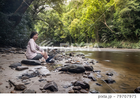 Tourist admiring scenic nature view of Tahan River bank with lush rainforest foliage at Taman Negara National Park, Pahang Tourist admiring scenic nature view of Tahan River bank with lush rainforest foliage at Taman Negara National Park, Pahang 79707975