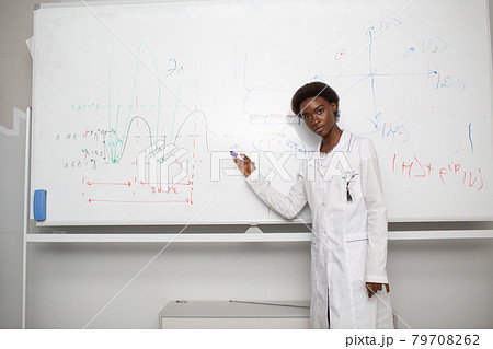 African American woman math teacher stands at blackboard with marker African American woman math teacher stands at blackboard with marker 79708262