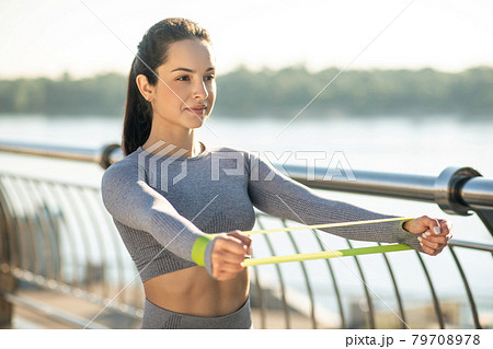 Young girl in grey sportswear training her arms with a resistance band 79708978