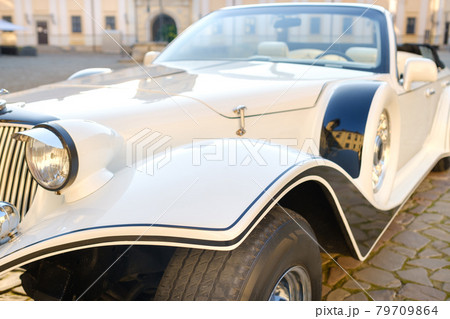 Close-up of the front of a white vintage car in the courtyard of the castle Close-up of the front of a white vintage car in the courtyard of the castle 79709864