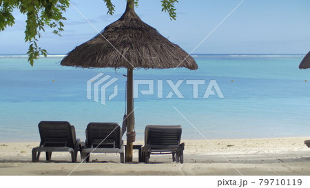 View of empty chaise-longue near native sun umbrella against blue water, Mauritius Island View of empty chaise-longue near native sun umbrella against blue water, Mauritius Island 79710119