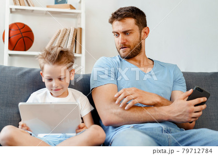 Worried father peeking at what his son is watching on digital tablet Worried father peeking at what his son is watching on digital tablet 79712784