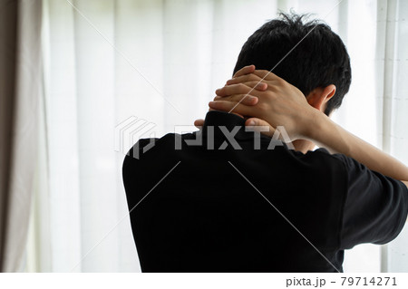 首に両手を置き窓辺に立つ男性の後ろ姿 79714271