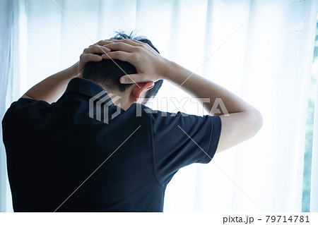 頭を抱えて窓辺に立つ男性の後ろ姿 79714781