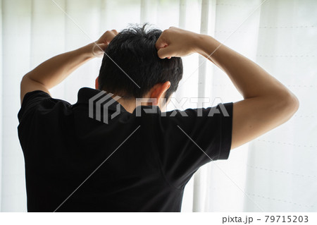 両手のげんこつを頭に添えて窓辺に立つ男性の後ろ姿 両手のげんこつを頭に添えて窓辺に立つ男性の後ろ姿 79715203
