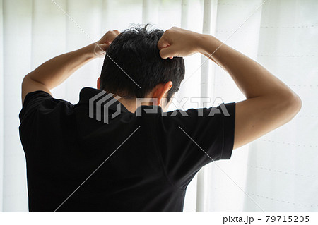 両手のげんこつを頭に添えて窓辺に立つ男性の後ろ姿 両手のげんこつを頭に添えて窓辺に立つ男性の後ろ姿 79715205