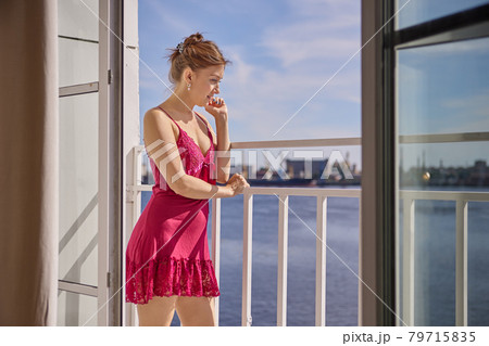 Woman in peignoir stands on loggia and looks out into street. 79715835