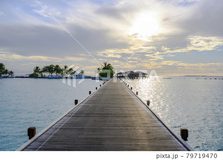 Boats, palm trees and a wooden pier stretching out into the ocean under the evening cloudy sky Boats, palm trees and a wooden pier stretching out into the ocean under the evening cloudy sky 79719470