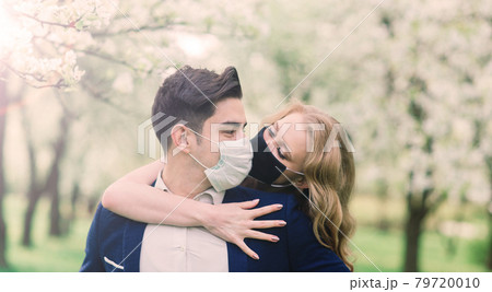 Young loving couple walking in medical masks in the park during quarantine on their wedding day. 79720010