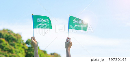 hand holding Saudi Arabia flag on blue sky background. September Saudi Arabia national day and Happy celebration concepts hand holding Saudi Arabia flag on blue sky background. September Saudi Arabia national day and Happy celebration concepts 79720145