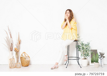 白い壁に置いてある椅子に座って、喉が痛いジェスチャーをする若い女性 白い壁に置いてある椅子に座って、喉が痛いジェスチャーをする若い女性 79720759