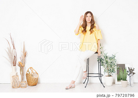 白い壁の前に置いてある椅子に座って、聞き耳を立てる若い女性 79720796