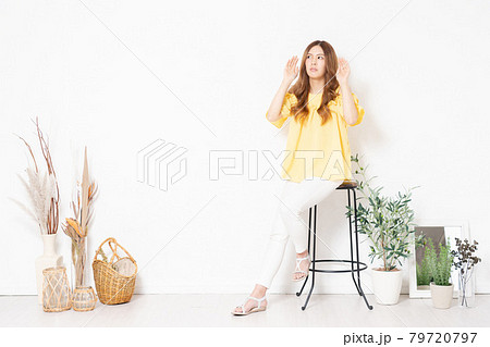 白い壁の前に置いてある椅子に座って、聞き耳を立てる若い女性 白い壁の前に置いてある椅子に座って、聞き耳を立てる若い女性 79720797