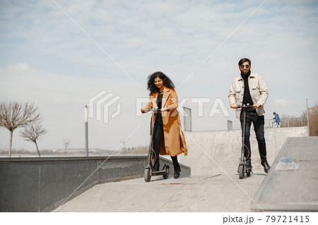 Interracial young couple with scooters in the city background Interracial young couple with scooters in the city background 79721415