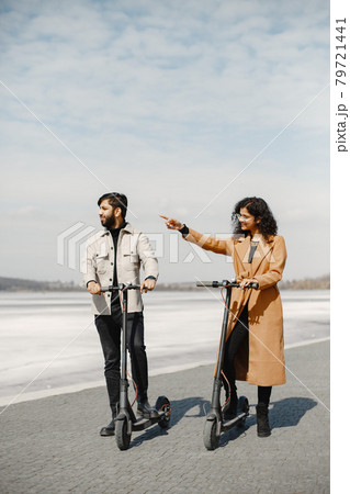 Interracial young couple with scooters in the city background Interracial young couple with scooters in the city background 79721441