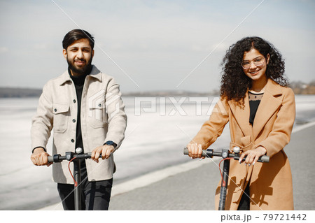 Interracial young couple with scooters in the city background Interracial young couple with scooters in the city background 79721442