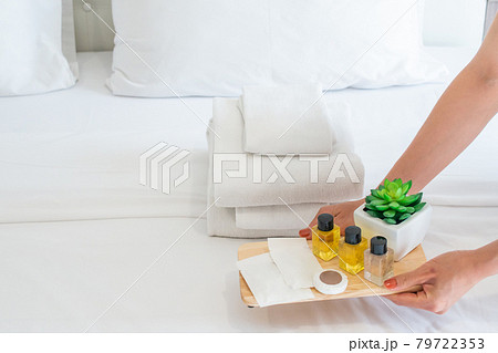 Hands of hotel maid put a set of hotel amenities (such as towels, shampoo, soap etc) on the bed. Hotel amenities is something of a premium nature provided in addition to the room when renting a room. Hands of hotel maid put a set of hotel amenities (such as towels, shampoo, soap etc) on the bed. Hotel amenities is something of a premium nature provided in addition to the room when renting a room. 79722353