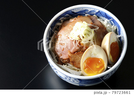 キャベツの千切りに味玉、ネギがトッピングされた焼豚丼を黒背景で俯瞰撮影 79723661