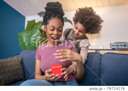 Enthusiastic african american woman and lovely daughter with gift. Enthusiastic african american woman and lovely daughter with gift. 79724276