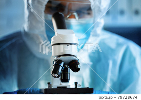 Medical worker in protective gown looking in microscope 79728674