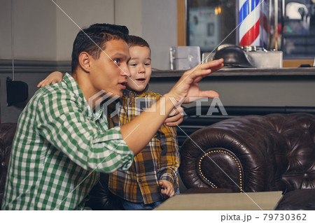 Young father and his stylish little son in the barbershop in the waiting room. 79730362
