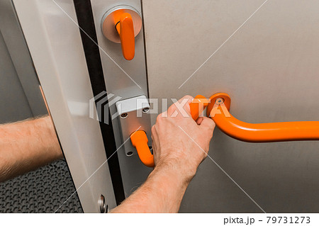 A man's hand holds on to a metal handle next to a handrail and opens a door in a modern electric train 79731273
