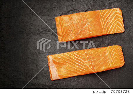 Two slices of salmon with on a black background with copy space, overhead photo Two slices of salmon with on a black background with copy space, overhead photo 79733728