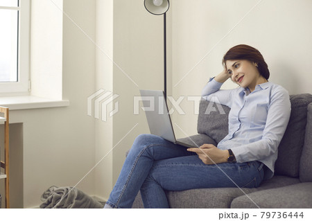Smiling millennial woman looking at laptop screen relax on couch at home 79736444