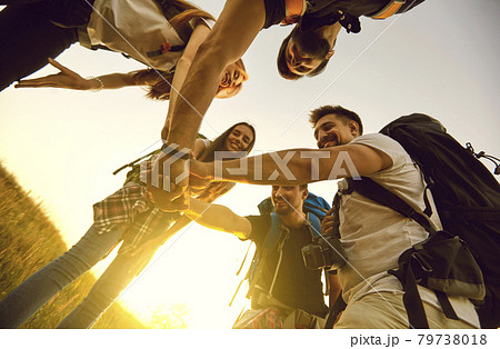 Low angle of team of tourists with rucksacks joining hands in field while hiking in countryside 79738018
