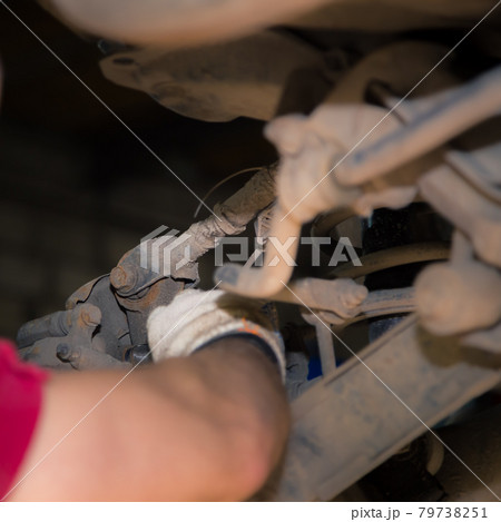 The man's hands unscrew the silent block in the chassis of the car.  79738251