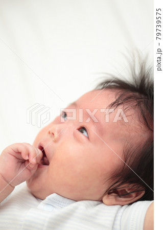 ベッドで寝転んで指しゃぶりをする赤ちゃんの女の子 79739575