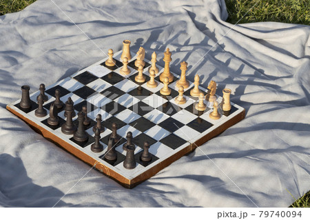 Old wooden chessboard with pieces in the park on gray blanket. Old wooden chessboard with pieces in the park on gray blanket. 79740094