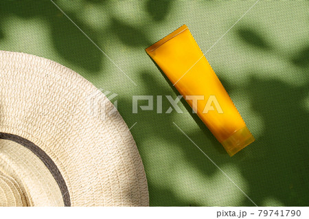Flat lay rafia hat and orange cosmetic tube on green texture botanical shadows 79741790