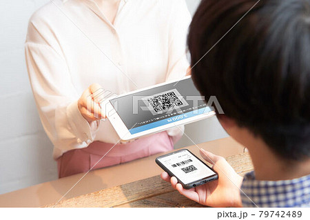 スマホに表示したQRコードをタブレットで読み取る店員の手元 79742489