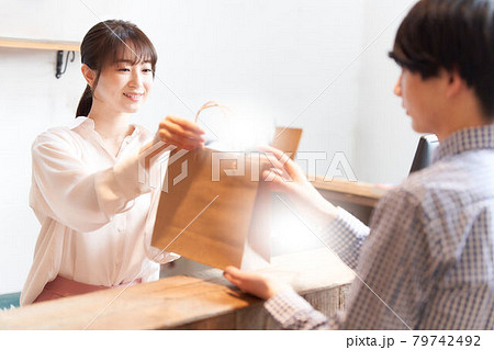 紙袋に入れた商品をお客に手渡す女性スタッフ 79742492
