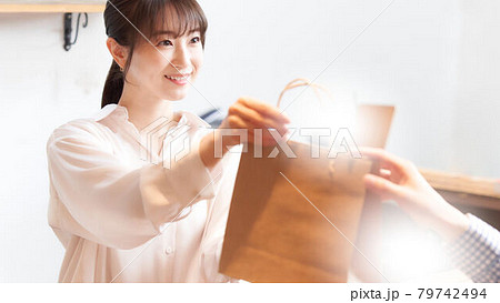 紙袋に入れた商品をお客に手渡す女性スタッフ 79742494