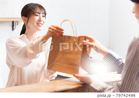 紙袋に入れた商品をお客に手渡す女性スタッフ 79742496