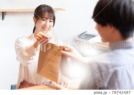 紙袋に入れた商品をお客に手渡す女性スタッフ 79742497