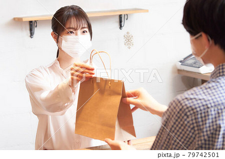 紙袋に入れた商品を渡すマスク姿の店員 紙袋に入れた商品を渡すマスク姿の店員 79742501