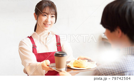 カウンターで注文品をお客に渡すカフェの女性店員 79742504
