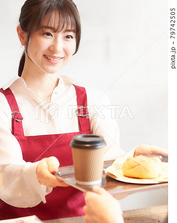 カウンターで注文品をお客に渡すカフェの女性店員 79742505