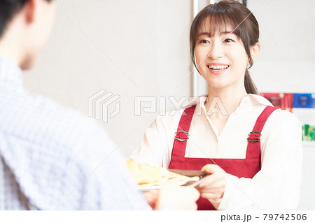 カウンターで注文品をお客に渡すカフェの女性店員 カウンターで注文品をお客に渡すカフェの女性店員 79742506